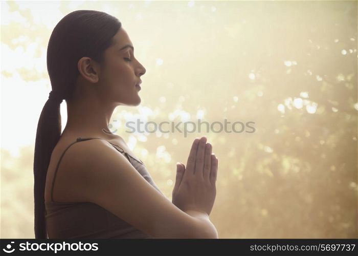 Side view of young woman with hands clasped meditating against trees