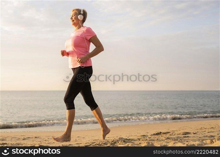side view older woman with headphones jogging beach
