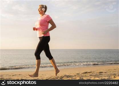 side view older woman with headphones jogging beach