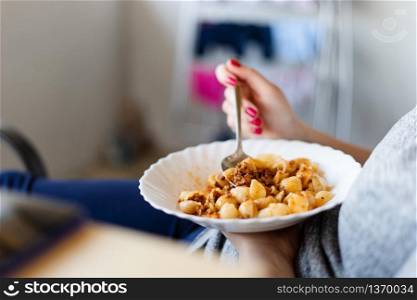 Side view on plate with pasta and meat sauce unknown female caucasian woman holding food in lap with spoon in other hand eating in day