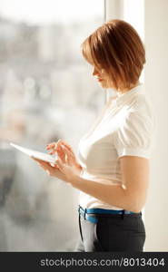 Side view on woman working on tablet near window in sunlight. Side view on woman working on tablet