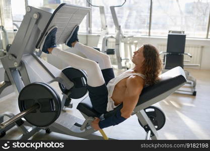 Side view on young man bodybuilder exercising legs muscles on gym machine. Hard full body training concept. Side view on young man bodybuilder exercising legs muscles on gym machine