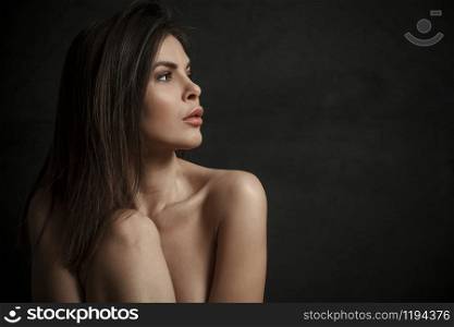 Side view portrait of a beautiful topless young woman over black background.