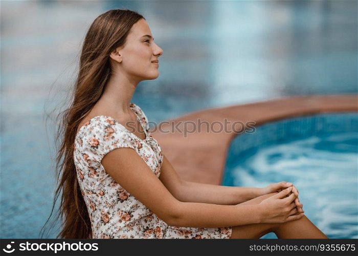 Side view portrait of a beautiful young female sitting near pool. Spending summer vacation on the beach resort. Happy holidays.. Attractive girl on the beach resort
