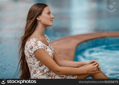 Side view portrait of a beautiful young female sitting near pool. Spending summer vacation on the beach resort. Happy holidays.. Attractive girl on the beach resort