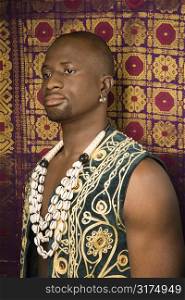 Side view portrait of African-American mid-adult man wearing embroidered African vest and beads.