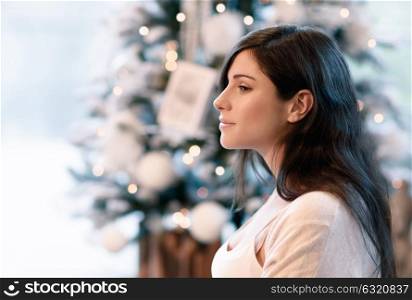 Side view portrait of beautiful brunet girl near beautiful decorated Christmas tree, spending winter holidays at home