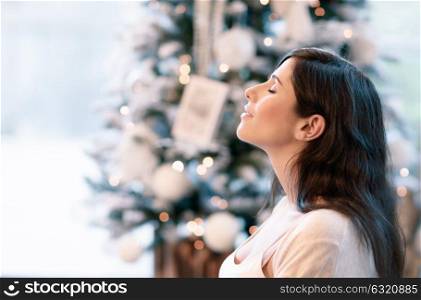 Side view portrait of beautiful brunet girl with closed eyes near beautiful decorated Christmas tree, with pleasure spending winter holidays at home