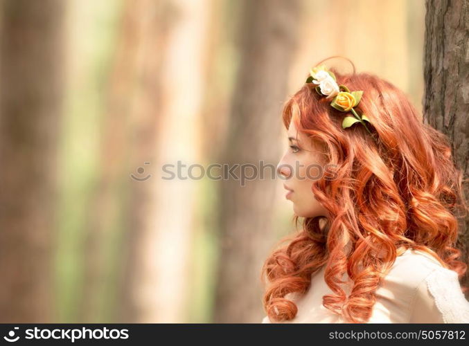 Side view portrait of beautiful redhead woman with gentle flower wreath in hair in the forest, fashion look, gorgeous hairstyle