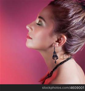 Side view portrait of gorgeous female with closed eyes over pink background, wearing elegant earrings and necklace, fashion look for Christmas party
