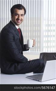 Side view portrait of happy businessman having coffee at office desk