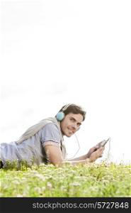 Side view portrait of man listening to music on MP3 player using headphones in park against clear sky