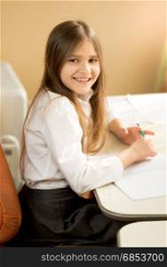 Side view portrait of smiling schoolgirl writing at exercise book