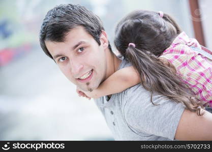 Side view portrait of young man piggybacking little daughter at home