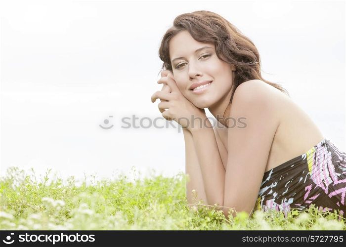 Side view portrait of young woman lying on grass against clear sky