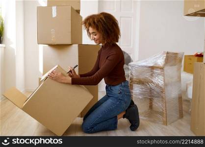 Side view portrait of young woman signing cardboard box with belongings while moving to new house. Side view portrait woman signing cardboard box