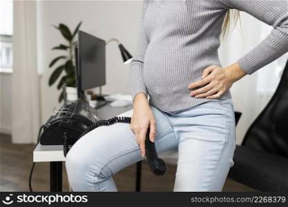 side view pregnant businesswoman sitting desk holding phone receiver