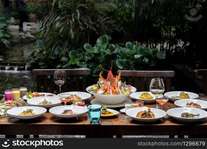 Side view premium variety of international food in garden of restaurant of lobster shrimp steak beef lamb pasta spaghetti risotto rice sushi sashimi and wine using for buffet food drink background.