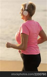 side view senior woman with headphones jogging beach