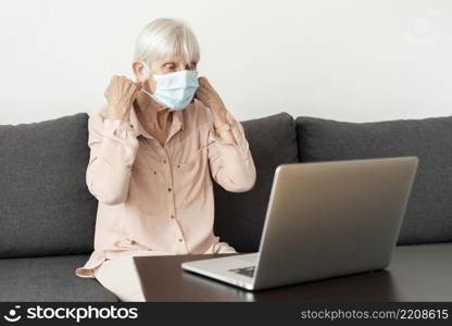 side view senior woman with laptop putting medical mask