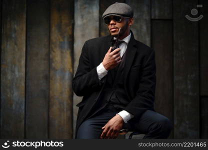 side view shot of stylish afro man in beautiful coat and glasses. Studio shot of stylish african american man wearing coat, cap, glasses and holding smoking pipe