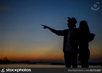Side view silhouette of a young couple standing near the lake with twilight, The lover have romantic moment with sunset in blue hour