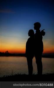 Side view silhouette of a young couple standing near the lake with twilight, The lover have romantic moment with sunset in blue hour