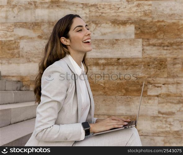 side view smiley businesswoman with smartwatch working laptop outdoors