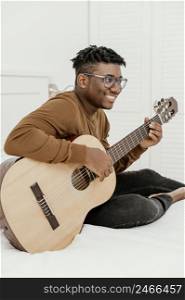 side view smiley male musician home playing guitar bed