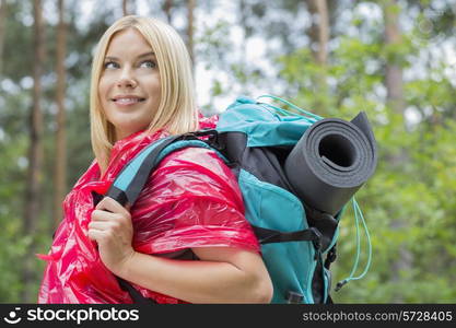 Side view smiling female backpacker in raincoat looking away at forest