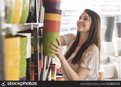 side view smiling young woman arranging flowering plants shelf