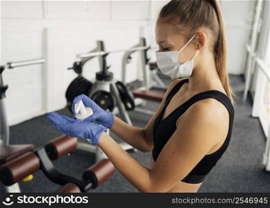 side view woman with medical mask gym using hand sanitizer gloves