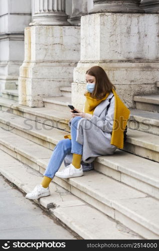 side view woman with medical mask sitting steps using smartphone