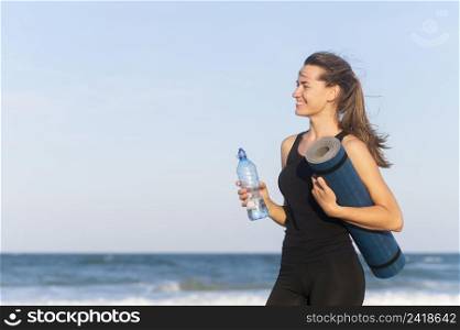 side view woman with water bottle yoga mat beach