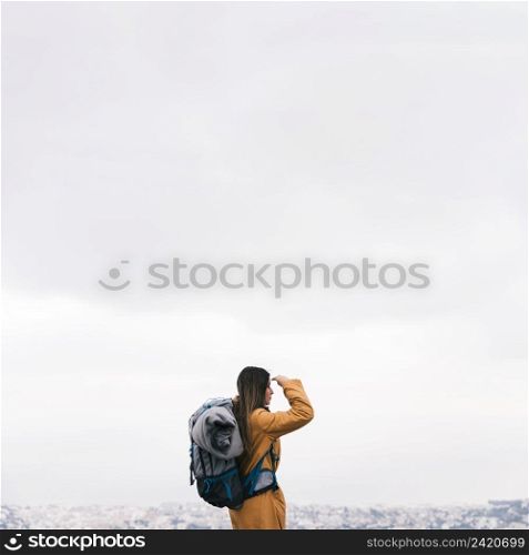 side view young female hiker with her backpack overlooking cityscape against sky