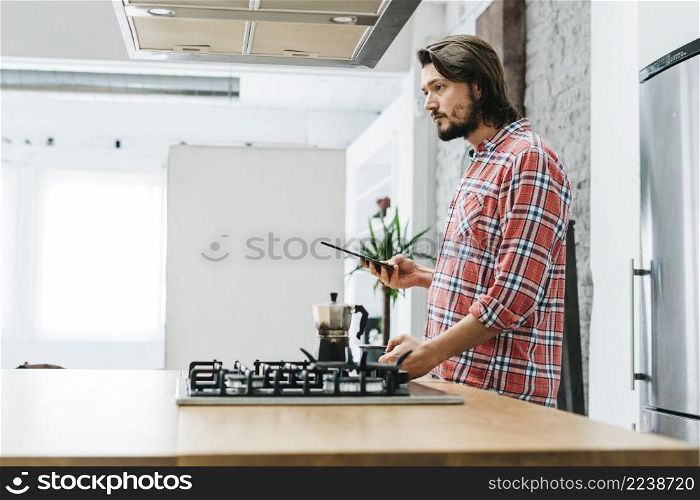 side view young man standing kitchen holding smart phone