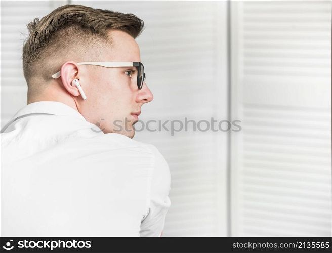 side view young man with white wireless earphone wearing eyeglasses looking away