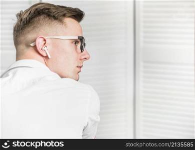 side view young man with white wireless earphone wearing eyeglasses looking away