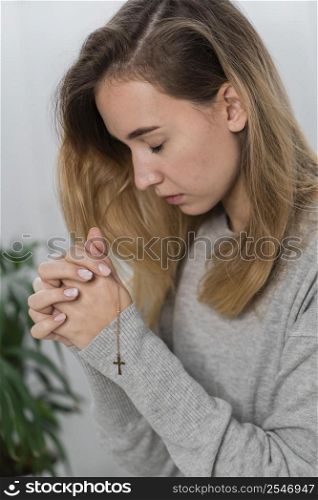 side view young woman praying with cross necklace