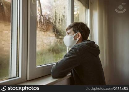 sideways boy with face mask looking through window