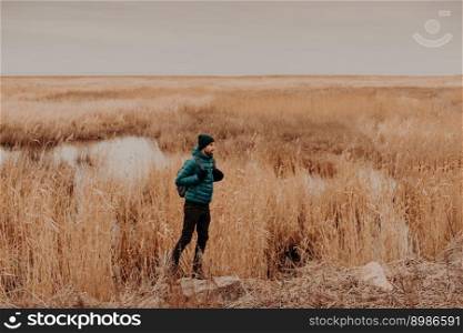 Sideways photo of attractive male dressed in fashionable hat, jacket and trousers, carries rucksack, stands outdoors, has unforgettable journey, enjoys autumn time. People, rest and lifestyle concept