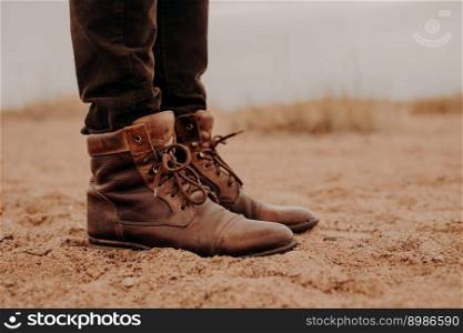 Sideways shot of man in shaggy brown shoes on lay surface. Pair of boots on sand. Male has outdoor walk in old footwear.