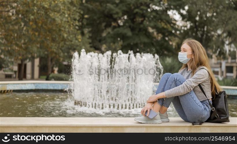 sied view woman wearing medical mask while sitting fountain