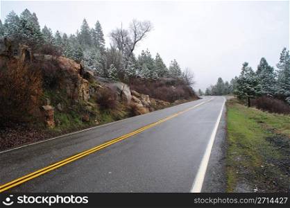 Sierra mountain road and yellow dividing line with trees and lite snow. Mountain Road
