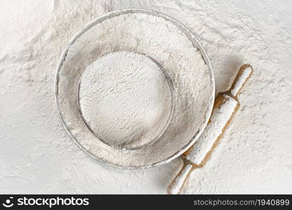 Sieve and a wooden rolling pin in flour. Top view. On a white background. . Sieve and a wooden rolling pin in flour. Top view.