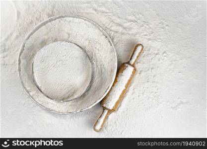 Sieve and a wooden rolling pin in flour. Top view. On a white background. . Sieve and a wooden rolling pin in flour. Top view.
