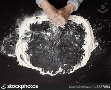 Sifted white wheat flour on a black table and two female hands, top view. cooking at home