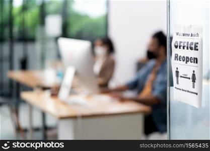 Signage of Office Reopen with social distancing practice with blurred background of Asian team business people working and wear face mask in new normal office to prevent covid-19 virus spreading.