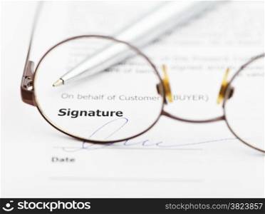 signature of sales agreement and silver pen through eyeglasses