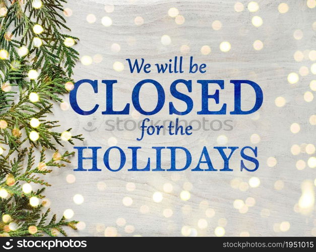 Signboard with the inscription We will be closed for the holidays and green branches of a Christmas tree. View from above, closeup, indoors, no people. Congratulations for family, friends, colleagues. We&rsquo;ll be closed for the holidays. Signboard